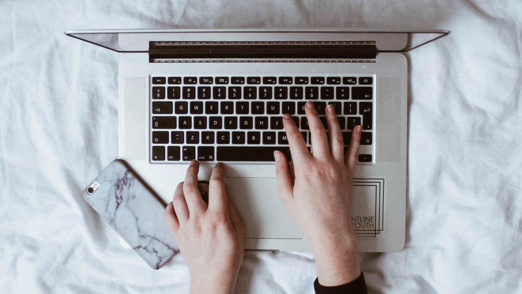 hands typing on a laptop on top of a duvet