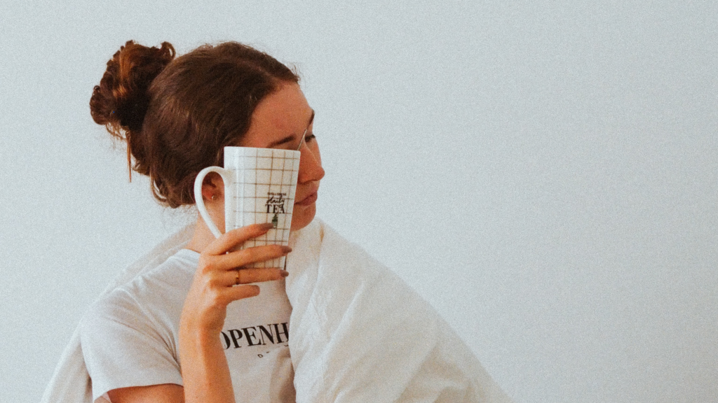 woman with a duvet over her shoulders holding a coffee mug to her face